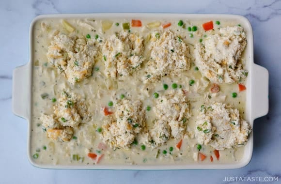 A white baking dish filled with pot pie filling and biscuits on top