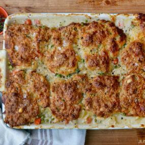 A baking dish with turkey pot pie and a towel and small dishes filled with herbs and salt