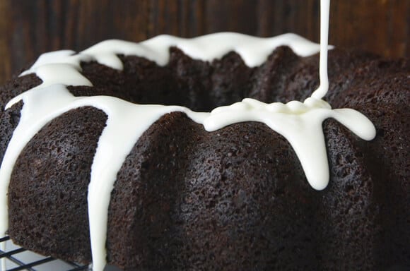 Vanilla glaze being drizzled over a dark chocolate gingerbread bundt cake.