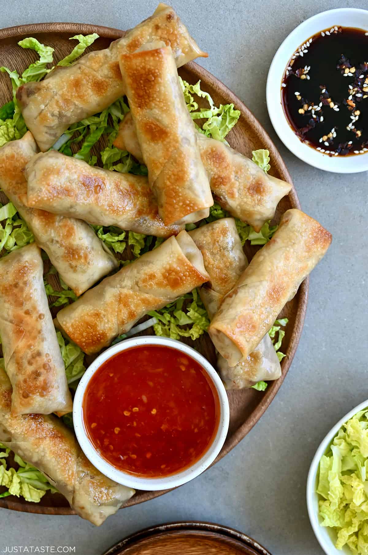 Crispy baked chicken spring rolls on a bed of shredded green cabbage next to a small bowl containing sweet chili sauce.