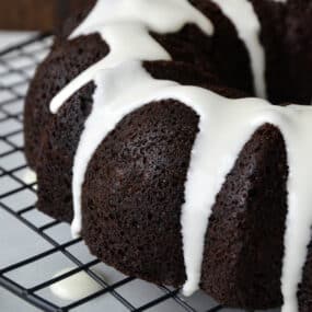 Chocolate gingerbread bundt cake drizzled with white glaze sits on a baking rack.