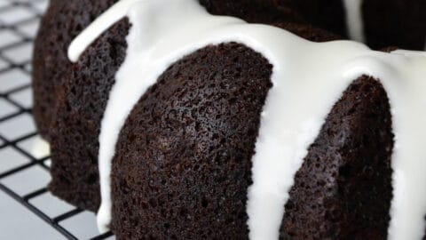 Chocolate gingerbread bundt cake drizzled with white glaze sits on a baking rack.