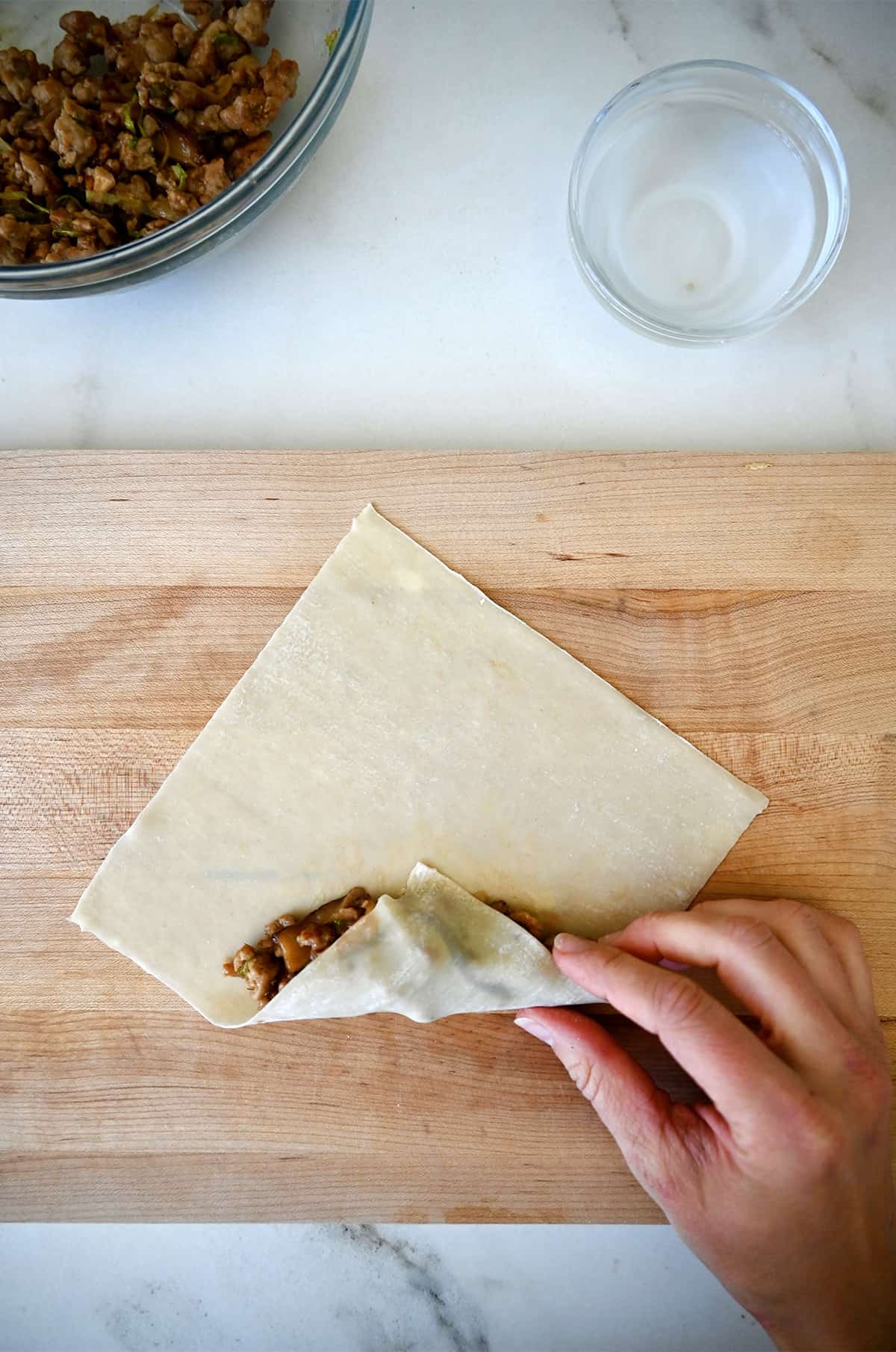 Step 2 in assembling a spring roll: Fold the bottom portion of the wrapper over the filling.