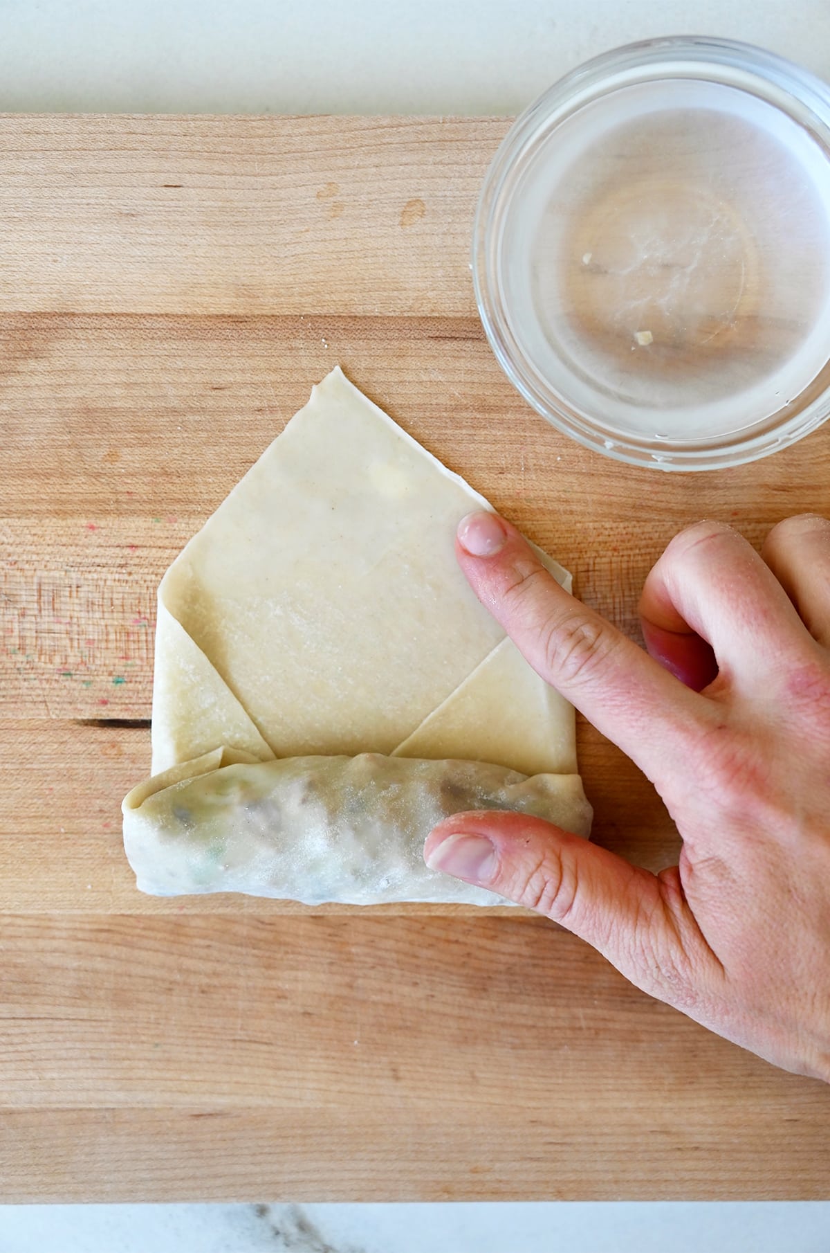 Step 4 in assembling a spring roll: Rolling the wrapper upwards and securing the edge with a little bit of water.