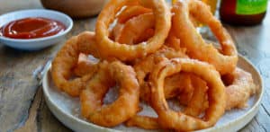 A plate of onion rings with Ranch dressing, ketchup and beer in the background