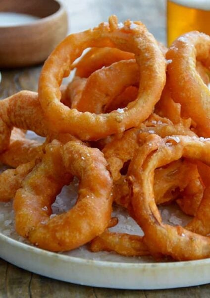 A plate of onion rings with Ranch dressing, ketchup and beer in the background