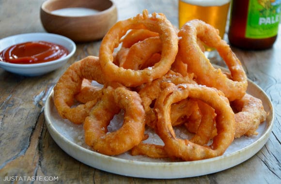 A plate of onion rings with Ranch dressing, ketchup and beer in the background