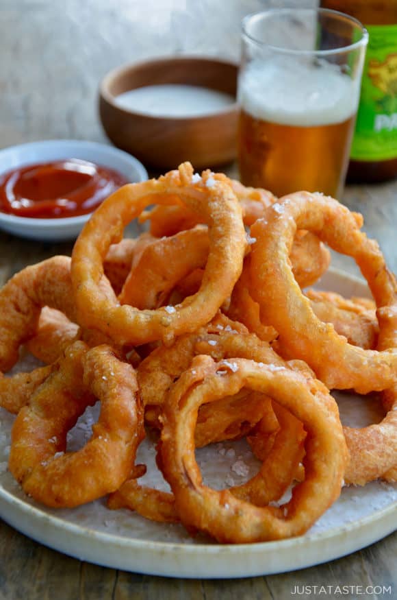 A plate of fried onion rings with beer and ketchup in the background