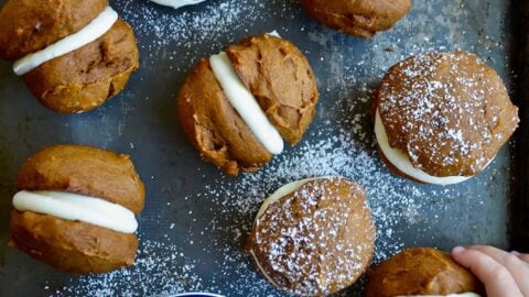 A baking sheet with whoopie pies and little kids' hands grabbing them