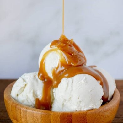 Easy Homemade Butterscotch Sauce poured over vanilla ice cream in wooden bowl