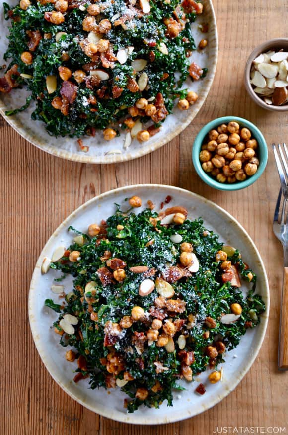 Two white plates piled high with kale salad with a small bowl of crispy chickpeas next to it