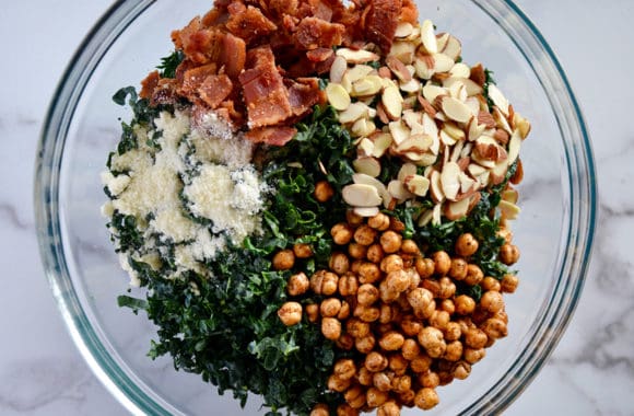 A glass bowl containing shredded kale, chickpeas, bacon, cheese and almonds