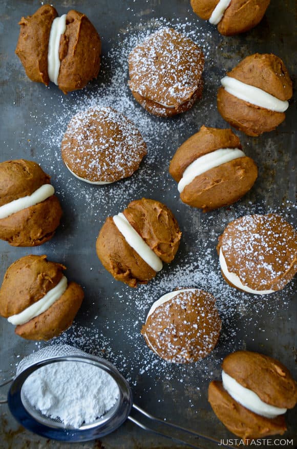 A baking sheet with pumpkin whoopie pies and a sieve with confectioners' sugar