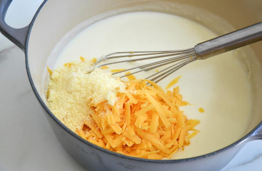 A large pot containing milk, parmesan and shredded cheddar cheese