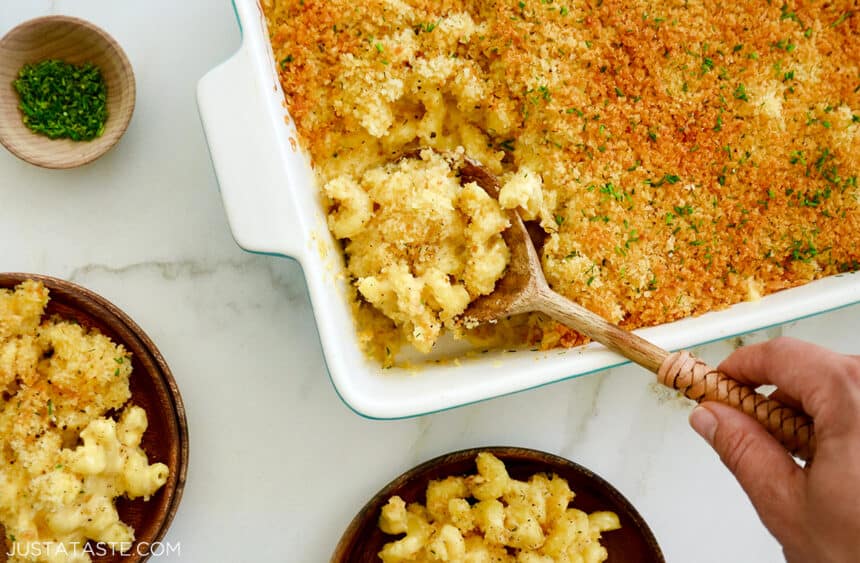 A hand holding a spoon in a baking dish with Roasted Garlic Macaroni and Cheese