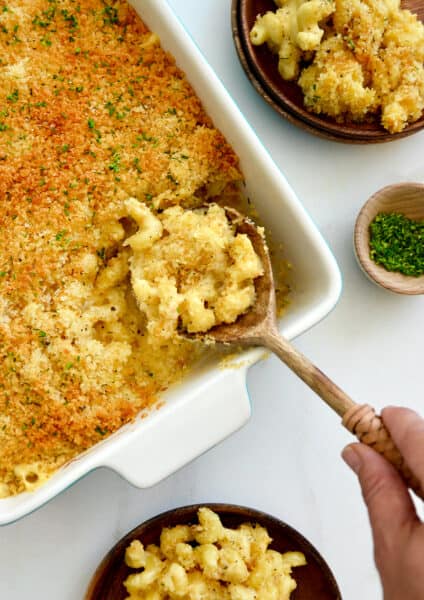 A hand holding a spoon in a baking dish of Roasted Garlic Macaroni and Cheese