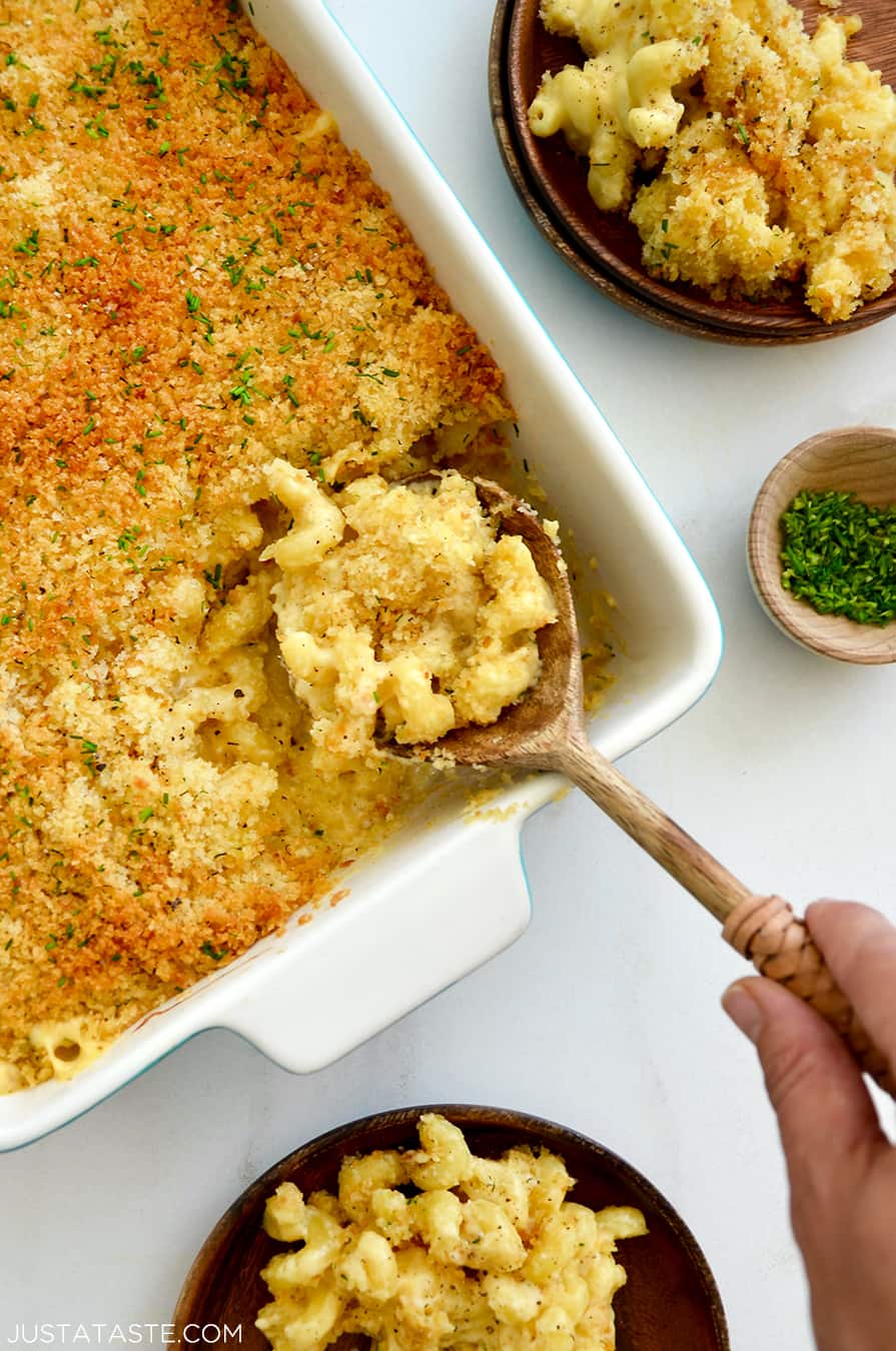 A hand holding a spoon in a baking dish of Roasted Garlic Macaroni and Cheese