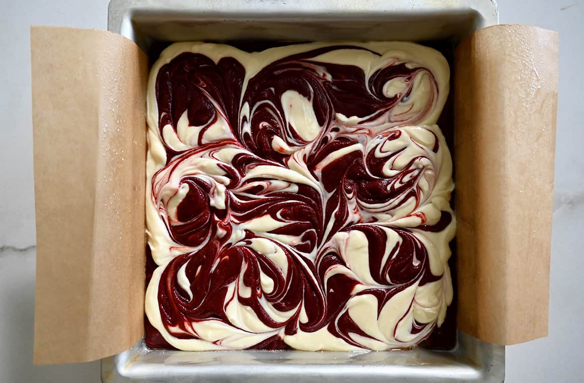 A top-down view of a parchment paper-lined baking pan with swirled cheesecake brownie batter