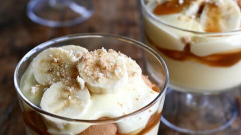 Three parfait glasses each filled with a layer of creamy banana pudding topped with salted caramel sauce, Nilla Wafers, sliced bananas and crushed wafers.