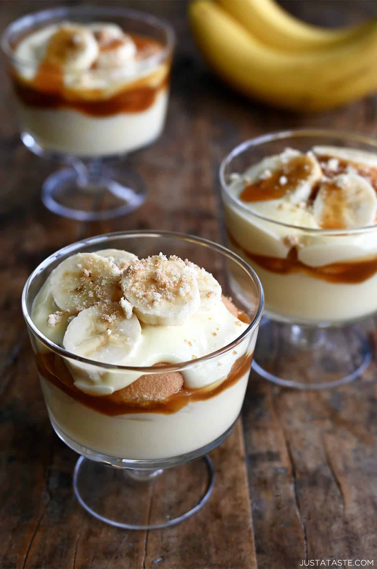 Three parfait glasses each filled with a layer of creamy banana pudding topped with salted caramel sauce, Nilla Wafers, sliced bananas and crushed wafers.