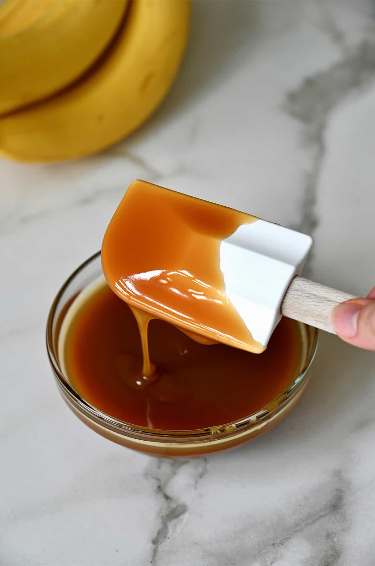 A spatula covered in salted caramel sauce over a small bowl filled with sauce.