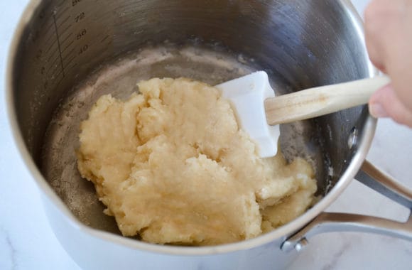 Hand holding spatula in small saucepan containing churro dough