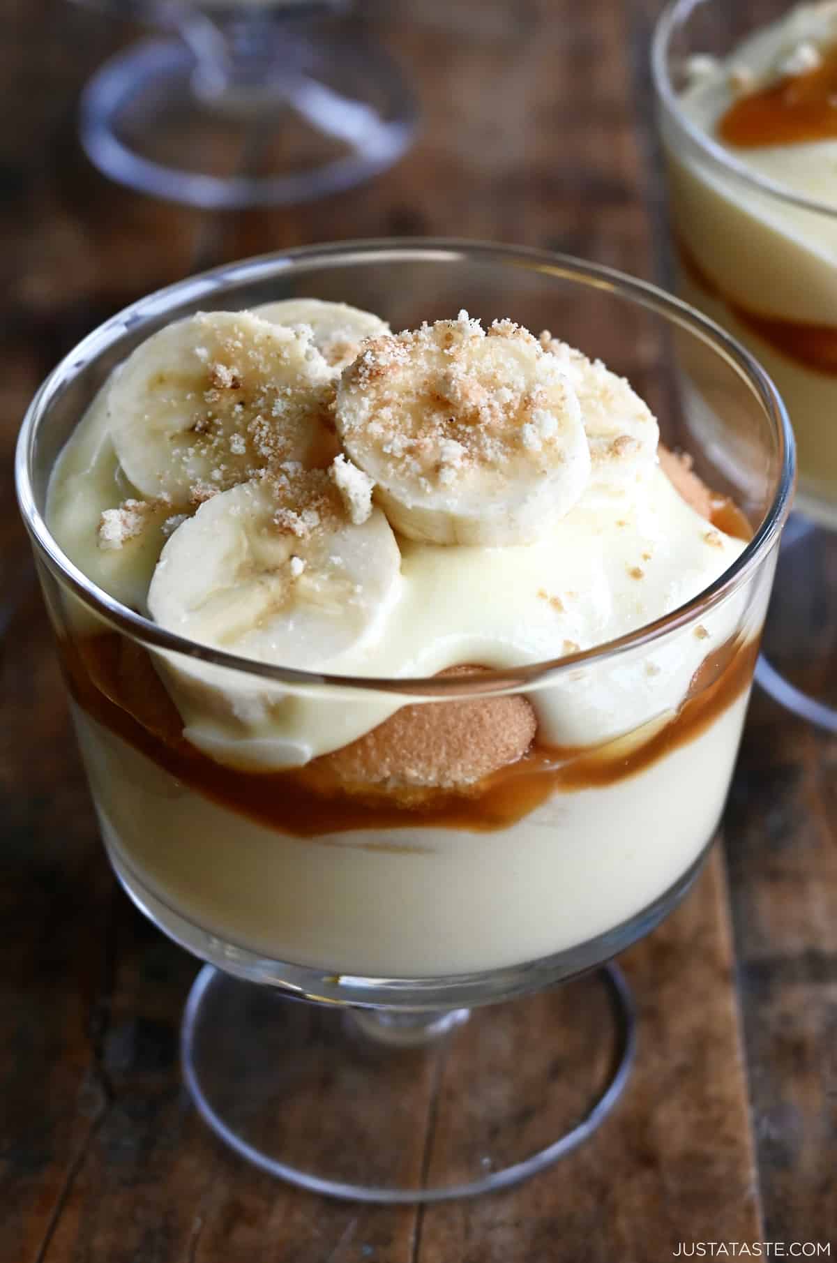 Banana pudding with salted caramel sauce, fresh sliced bananas and mini vanilla wafers in a parfait glass.