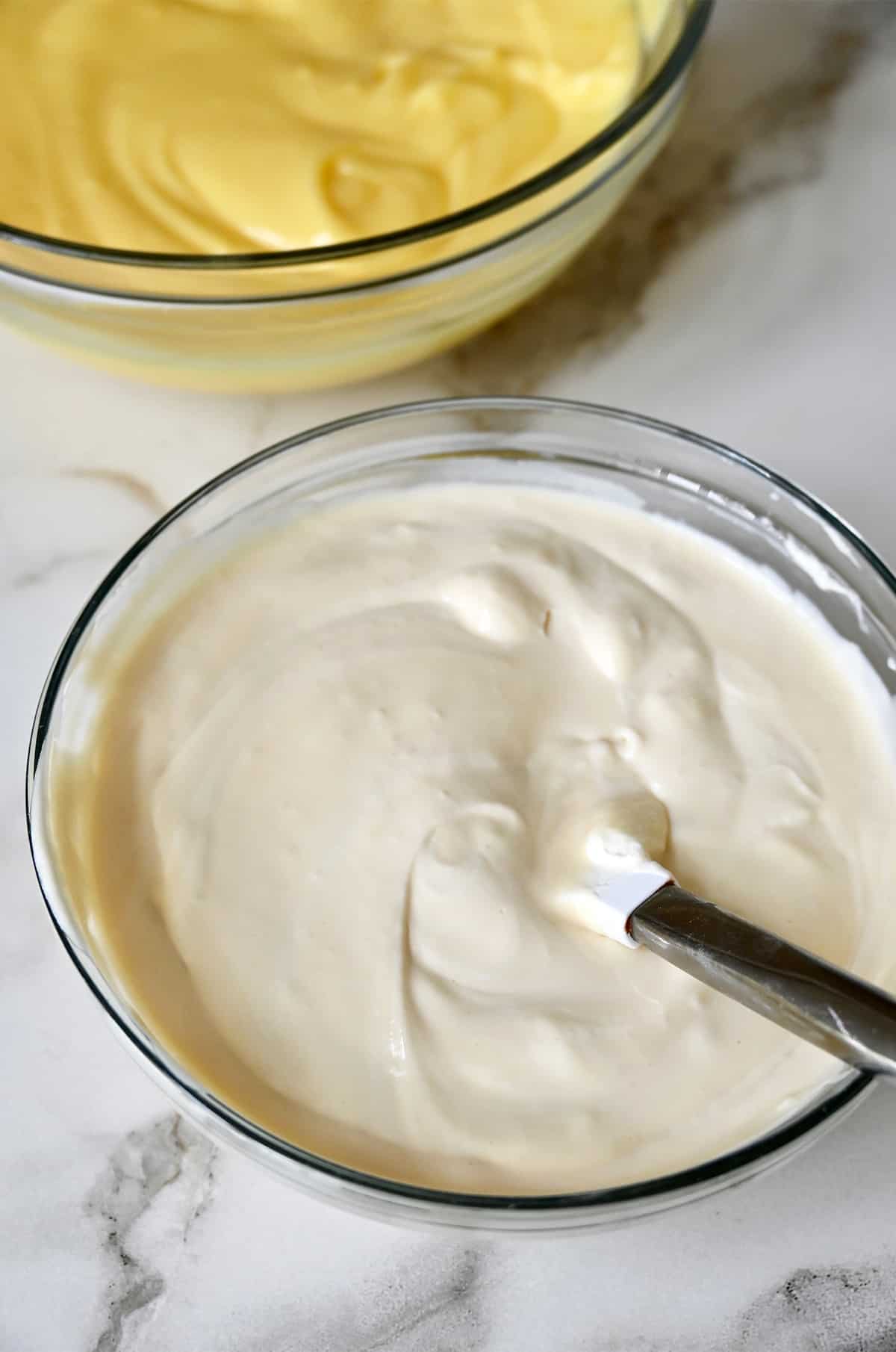 A glass bowl containing a mixture of cream cheese, sweetened condensed milk and whipped cream next to a glass bowl with banana pudding.