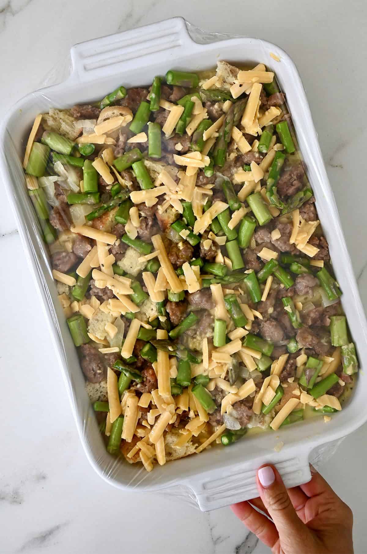 Unbaked sausage breakfast casserole covered with plastic wrap, ready to go into the fridge.