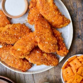 Crispy Baked Cheddar-Dijon Chicken Tenders on a white plate next to a small ramekin with ranch