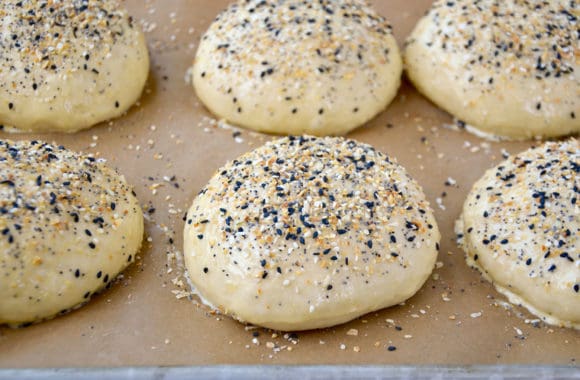 A baking sheet with unbaked burger buns on top