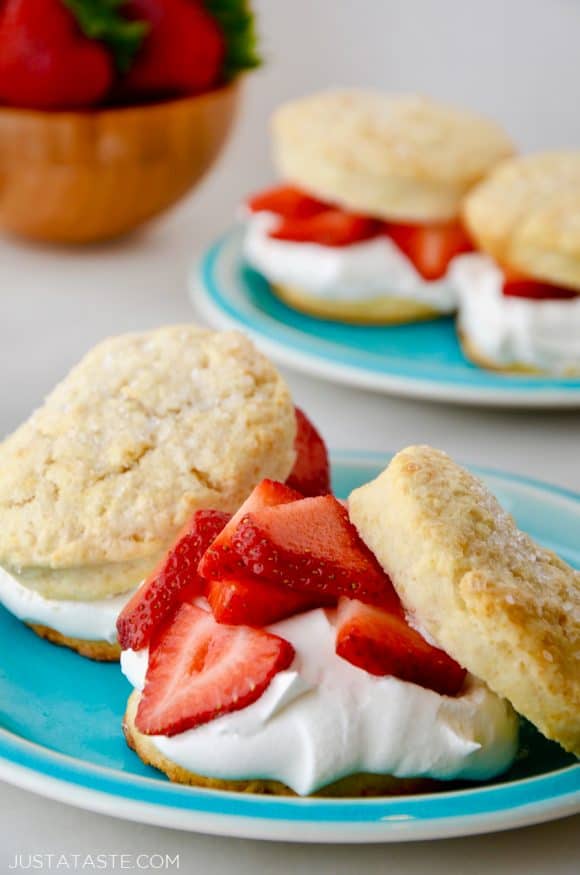 Easy Strawberry Shortcake on blue plate with wooden bowl filled with strawberries and more shortcakes on a blue plate in background.