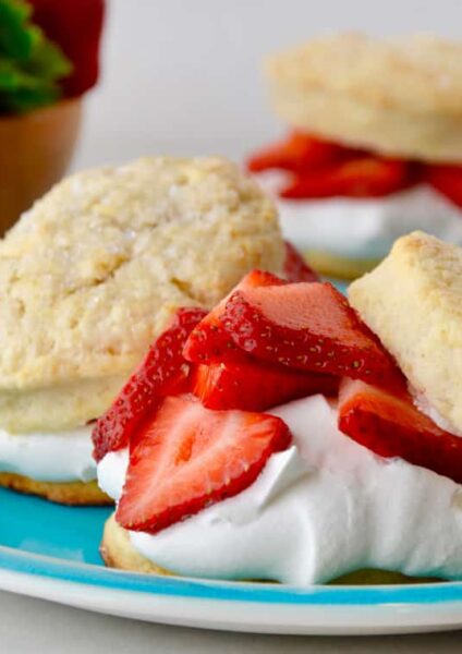 Easy Strawberry Shortcakes with homemade whipped cream on blue plate with small wooden bowl filled with fresh strawberries in background.
