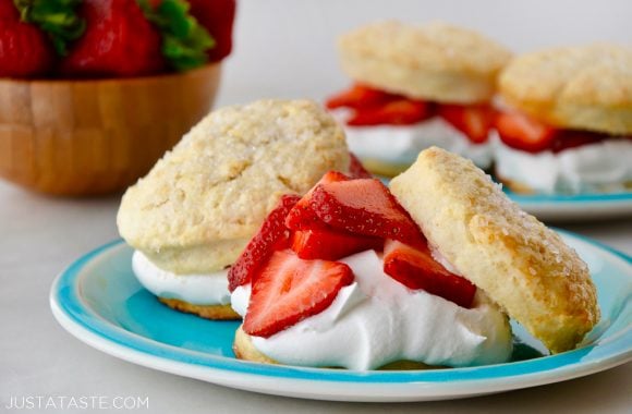 Easy Strawberry Shortcakes with homemade whipped cream on blue plate with small wooden bowl filled with fresh strawberries in background. 