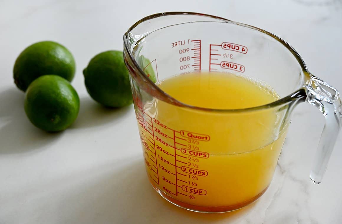 Boozy popsicle mixture in a glass measuring cup next to limes