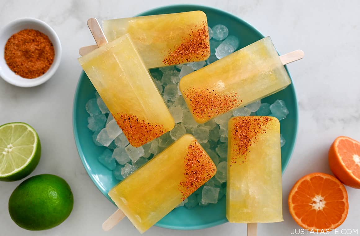 A top-down view of Skinny Margarita Popsicles with tajin seasoning over ice in a bowl next to a lime and an orange