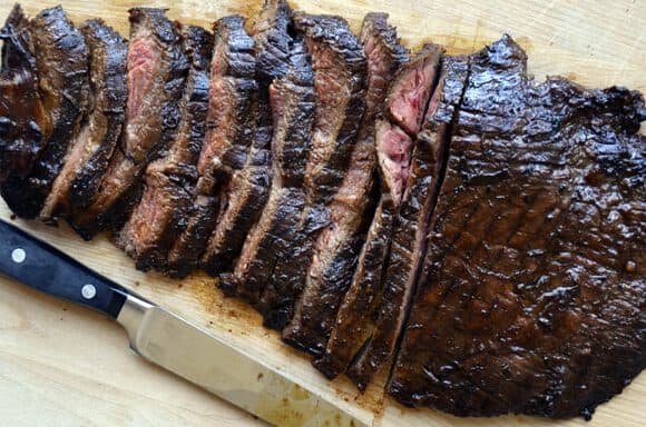 Sliced flank steak on cutting board with sharp knife