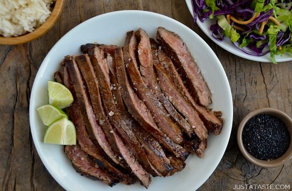 Sliced Asian flank steak on white servings plate with lime wedges