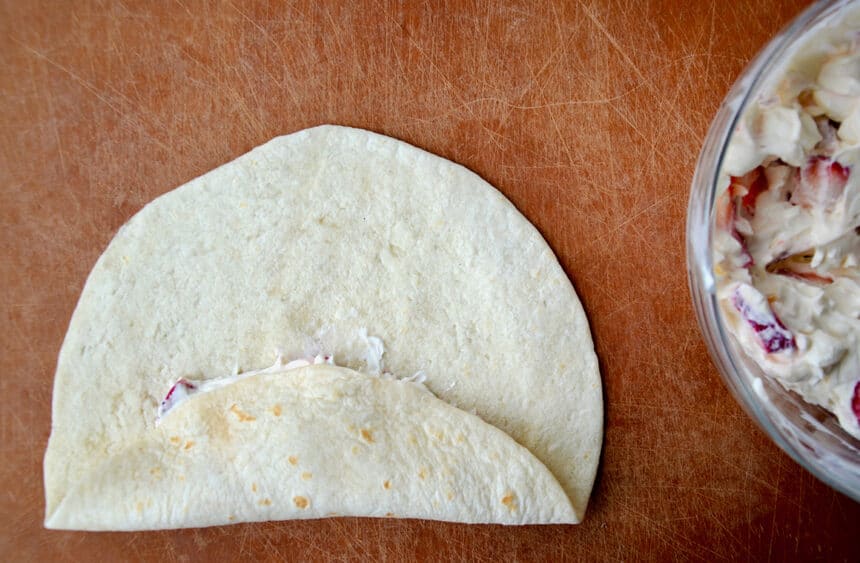 Flour tortilla folded over filling next to a bowl containing cream cheese and fresh fruit