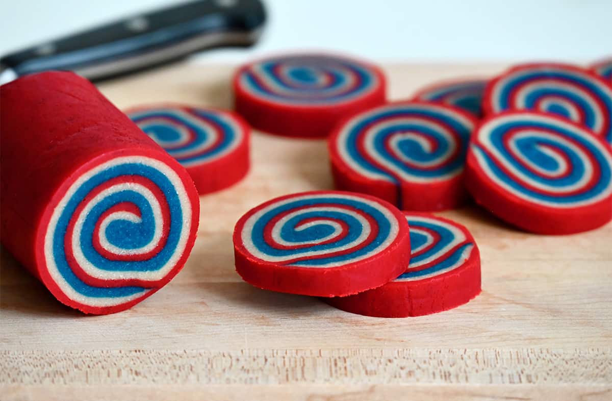 Red, white and blue slice-and-bake cookie dough sliced into rounds on a cutting board.