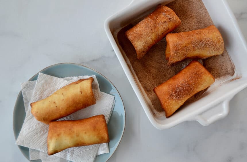 Deep-fried tortillas in a shallow dish being rolled in a cinnamon-sugar mixture