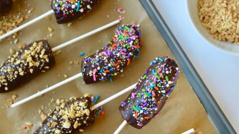 Top down view of child's hand grabbing a frozen banana with chocolate and sprinkles
