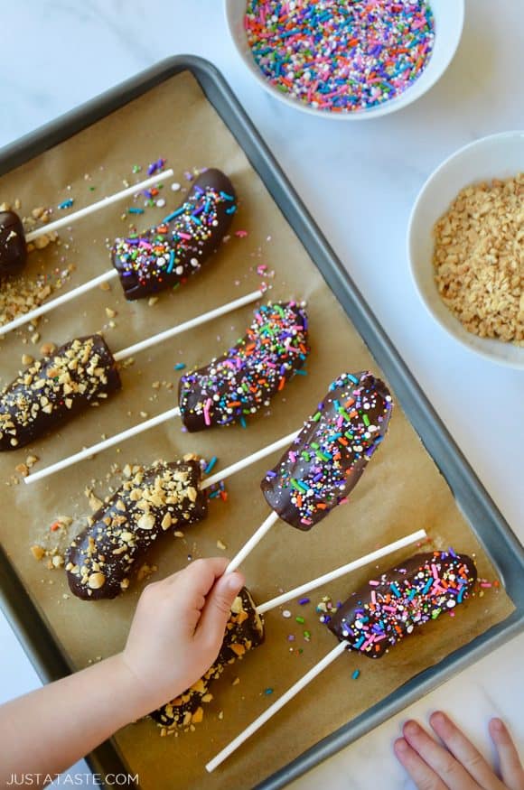 Top down view of child's hand grabbing a frozen banana with chocolate and sprinkles