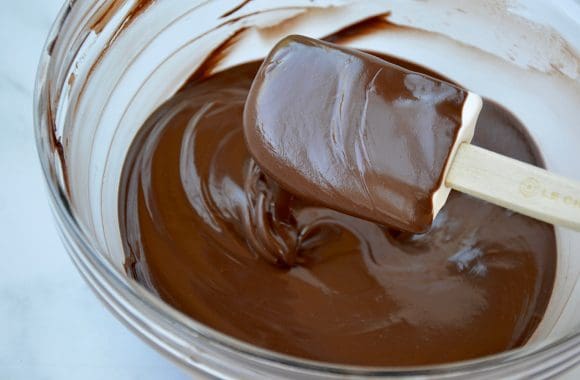 Spatula covered with melted chocolate over glass bowl containing melted chocolate