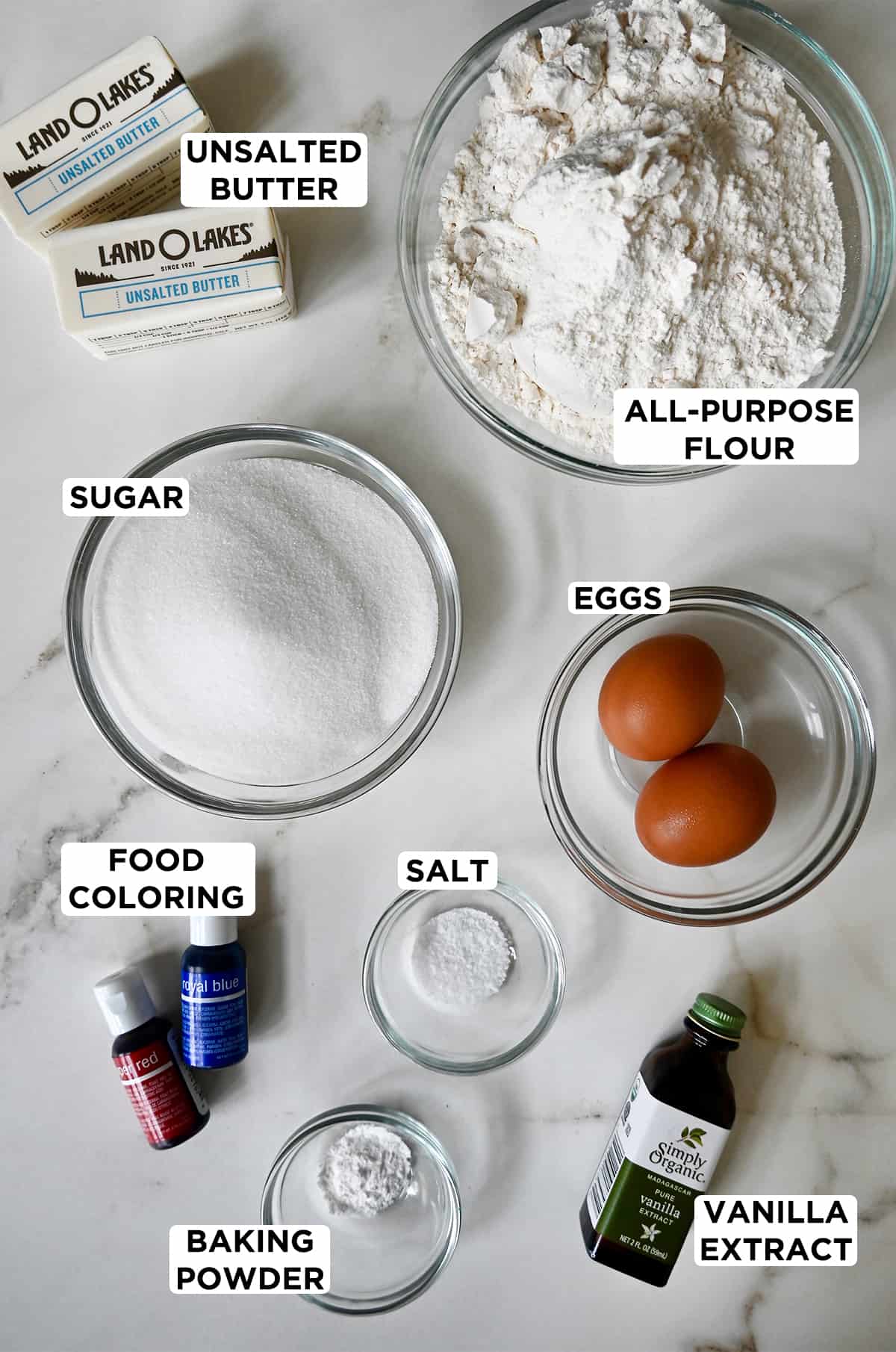 A top-down view of the ingredients needed to make pinwheel cookies, including butter, all-purpose flour, eggs, salt, vanilla extract, baking powder, sugar and food coloring.