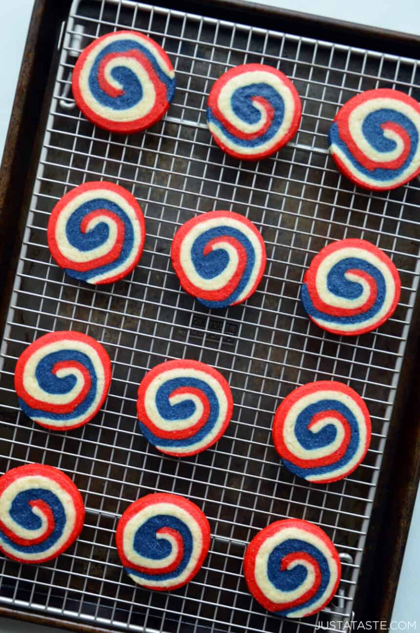 A top-down view of red, white and blue pinwheel icebox cookies atop a wire rack on a baking sheet