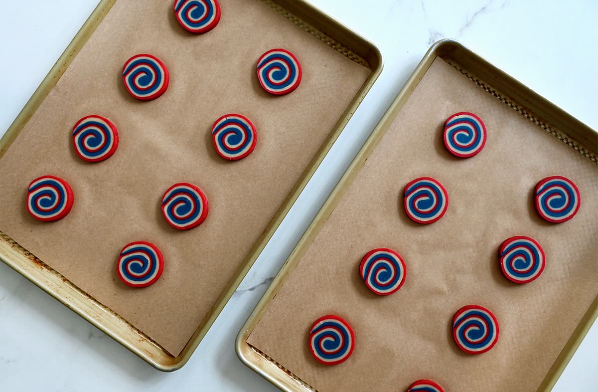 Two parchment paper-lined baking sheets with sliced cookie dough rounds.