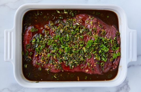 Flank steak in Asian marinade topped with minced garlic and ginger, and thinly sliced scallions