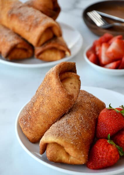 Two Strawberry Cheesecake Chimichangas on a white plate with fresh strawberries