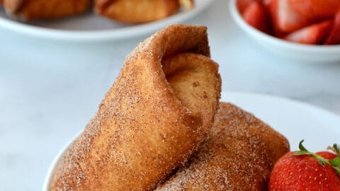 Two Strawberry Cheesecake Chimichangas on a white plate with fresh strawberries